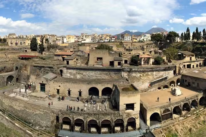 Panoramic view of ancient Hercolaneum ruins with Mount Vesuvius in the background, showcasing historical architecture.