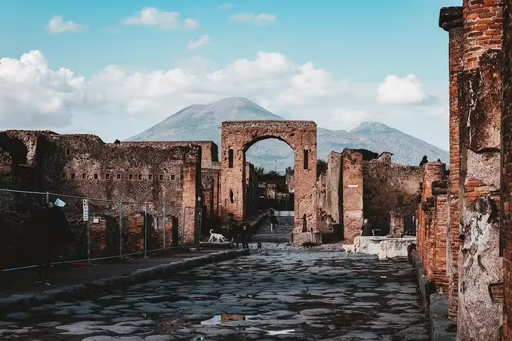 Ancient Herculaneum street with stone paving and archway, Mount Vesuvius view on tour from Naples
