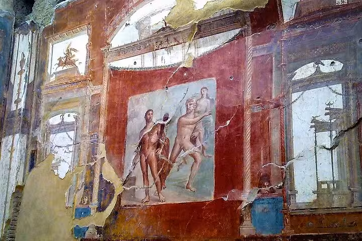 Fresco of classical figures in Herculaneum, illustrating Roman life and art on a weathered red wall.