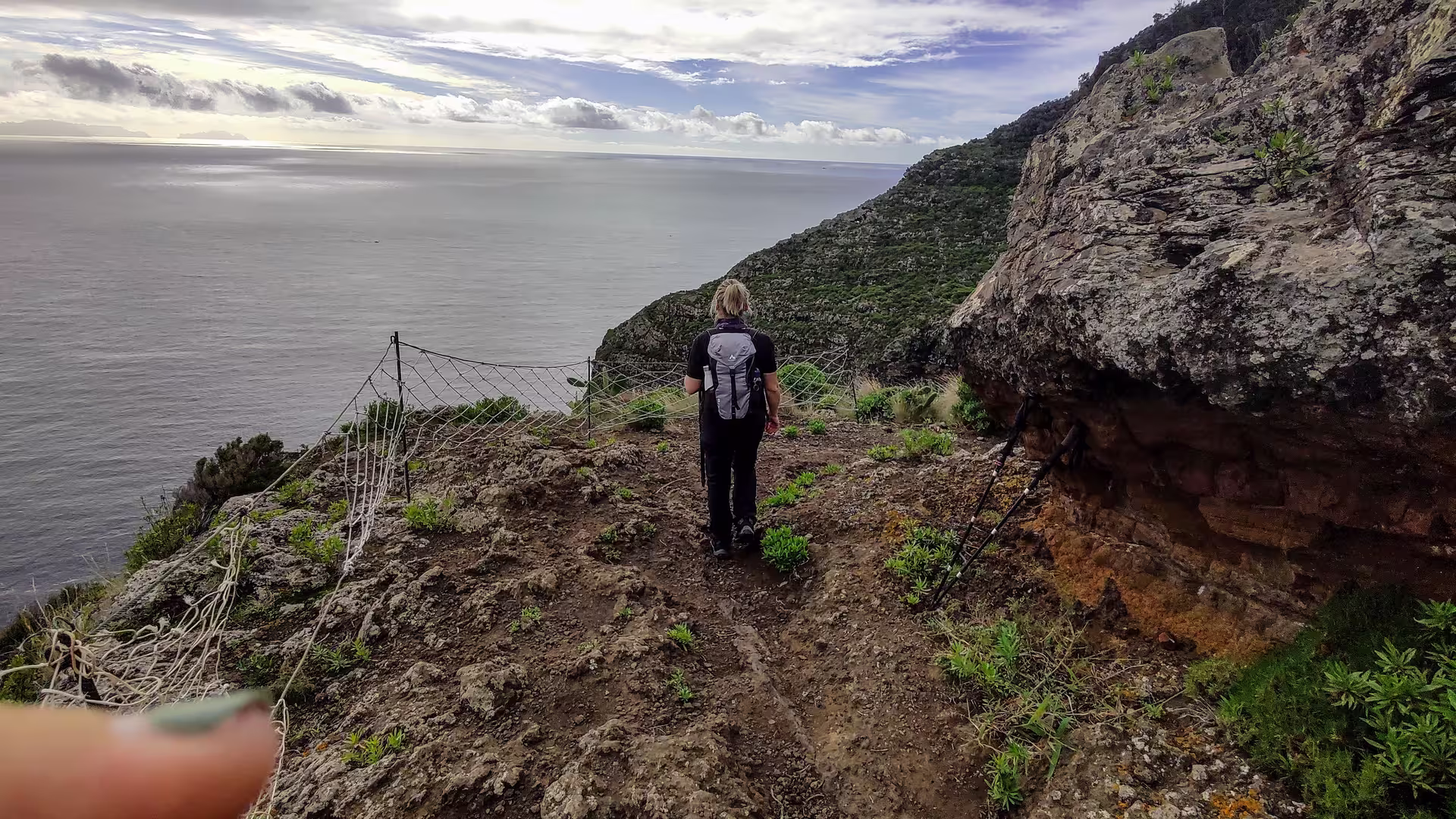 Hiker on rugged cliffside trail overlooking expansive ocean views during The Old Path's Hike adventure.