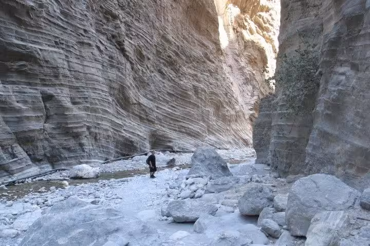 Hiker walking between towering cliffs in Samaria Gorge on a full-day tour from Rethymno, Crete