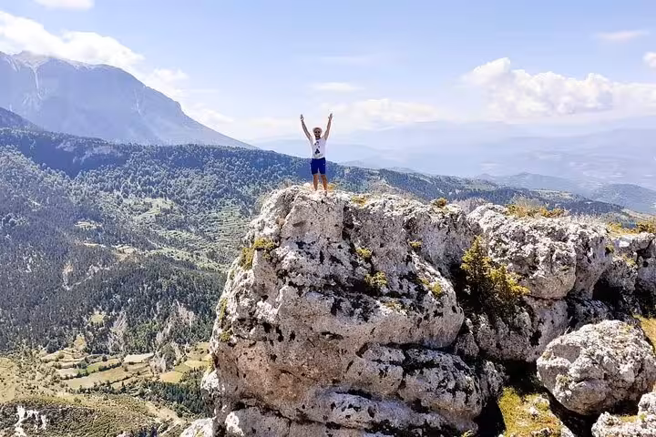 Hiker triumphantly stands atop a rugged rock formation at Tomor Mountain, showcasing breathtaking views of Dardhe's lush landscape.