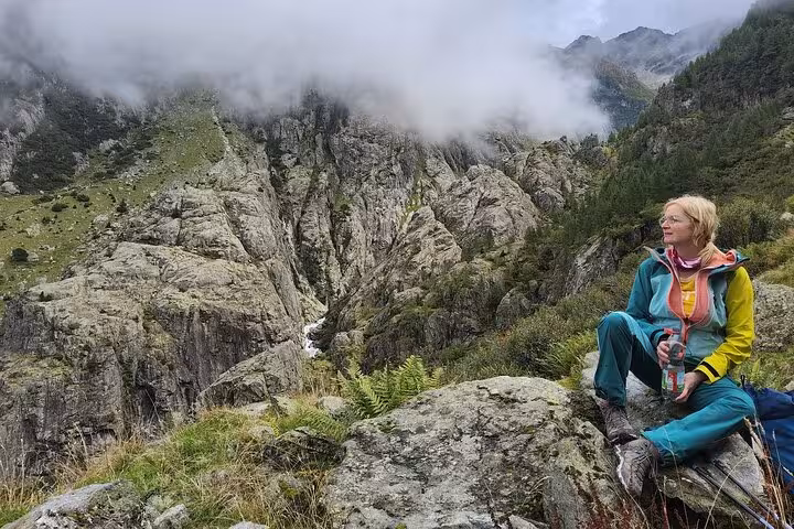 Hiker resting on rocky Swiss Alps trail near Trift Bridge, Zurich day trip with misty mountain views