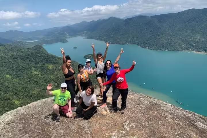 Group of hikers celebrate atop Peak Sugar Bread, capturing unforgettable views of vibrant forested mountains and clear waters.