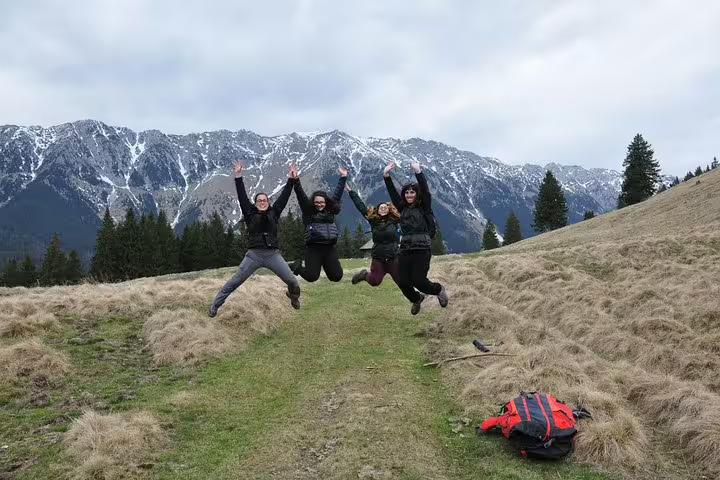 Four hikers jumping with joy on a mountain trail in Piatra Craiului National Park with snowy peaks behind