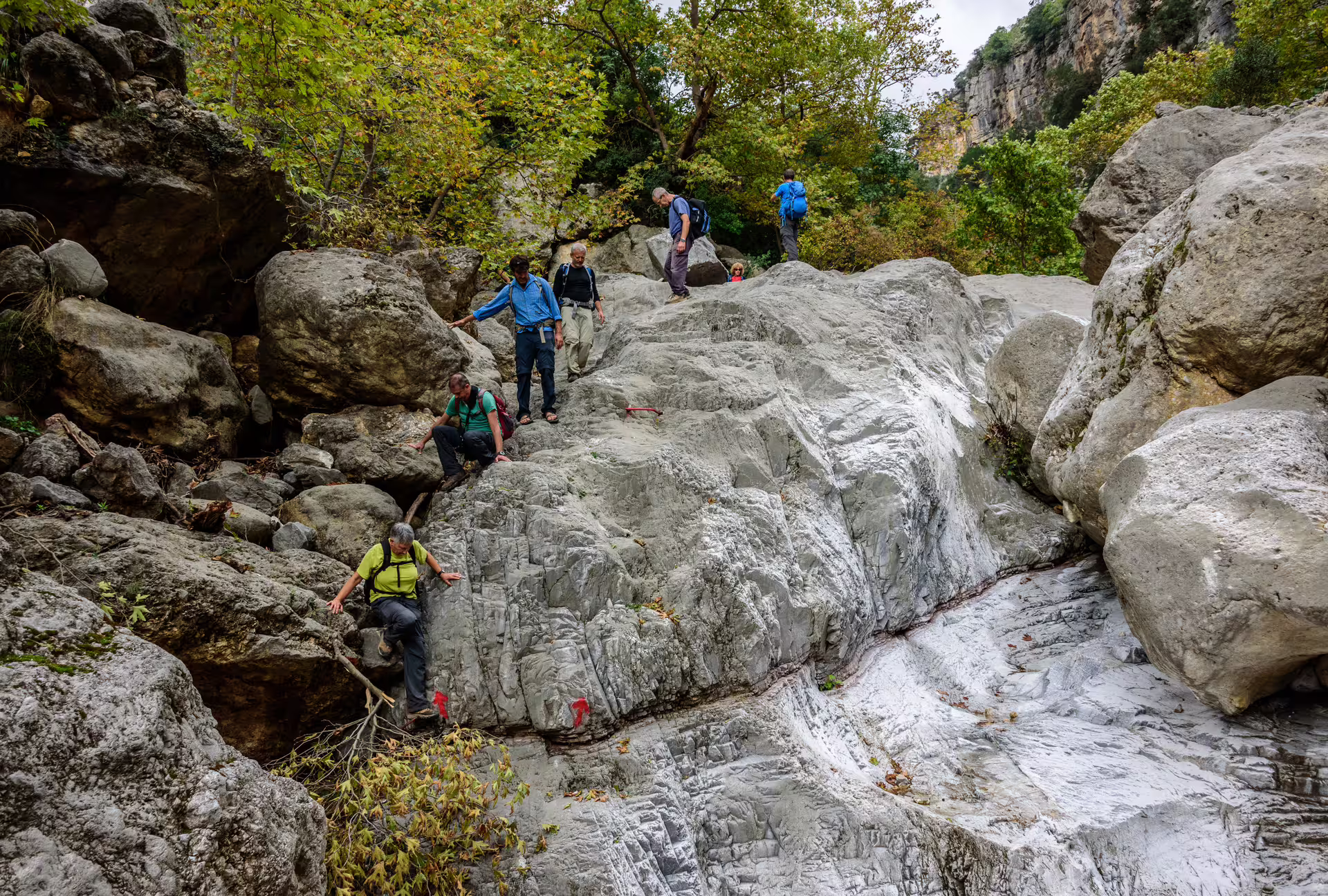 Hikers scrambling over smooth limestone boulders in Ridomo Gorge on a guided canyon hiking adventure in Greece