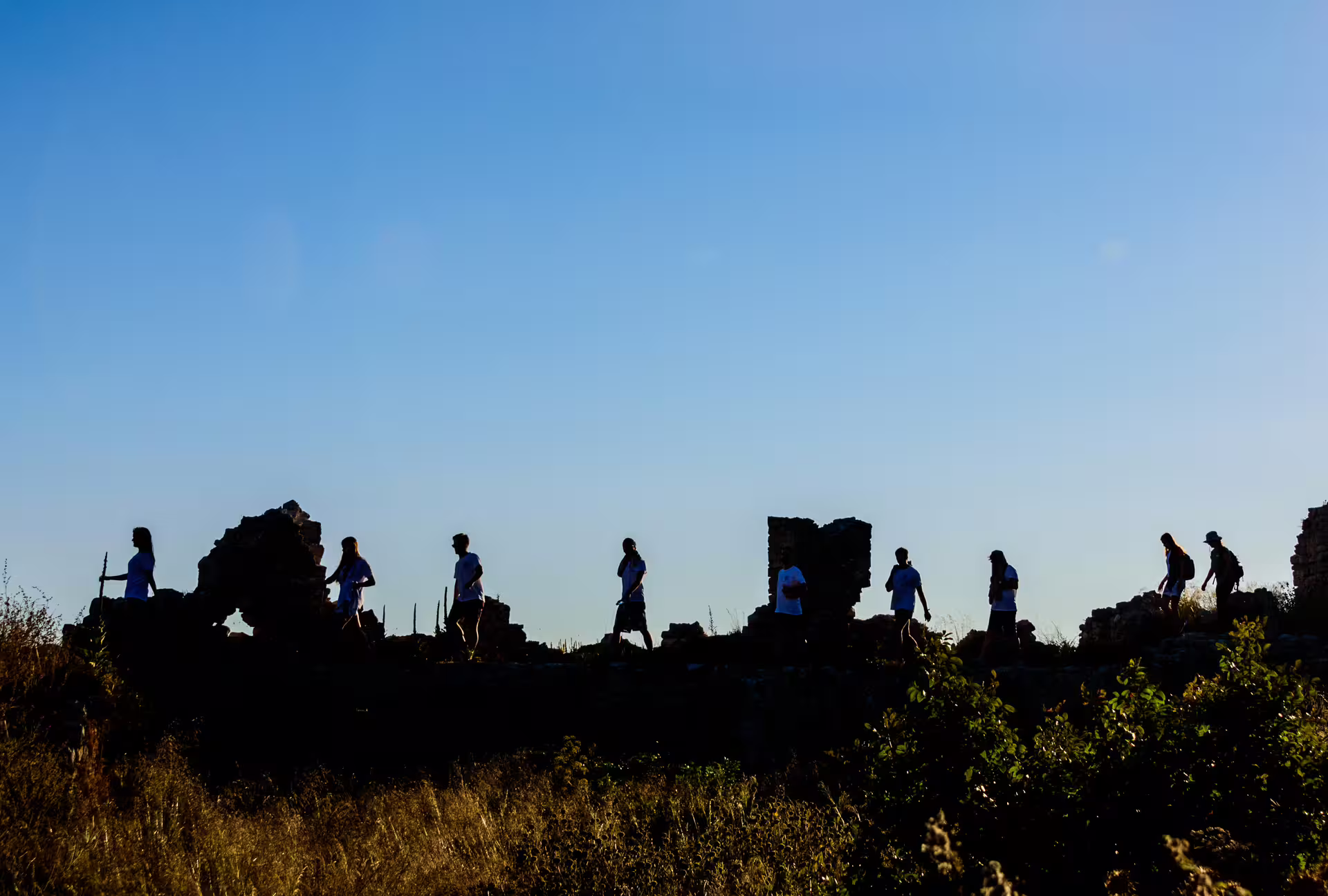 Silhouetted hikers exploring ruins at sunset near Navarino Bay, Pylos, on a small-group guided hike
