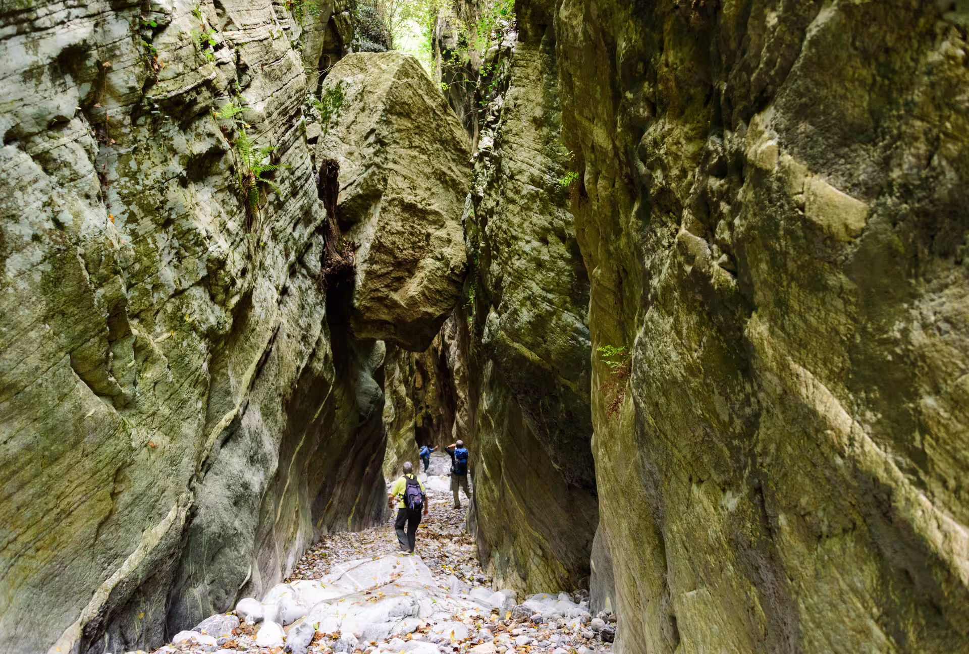 Hikers in narrow Ridomo Gorge canyon with towering cliffs and boulders on guided hiking tour in Greece
