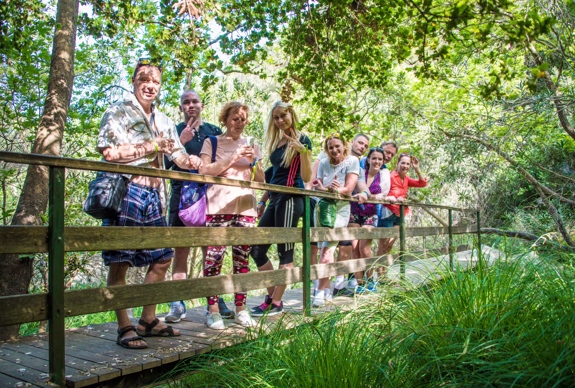 Group of hikers on a wooden bridge in lush forest on the Polylimnio Waterfalls hike, Messinia Greece