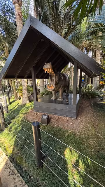 Lifelike hippopotamus sculpture under a wooden shelter in a lush garden setting for art and sculpture enthusiasts.