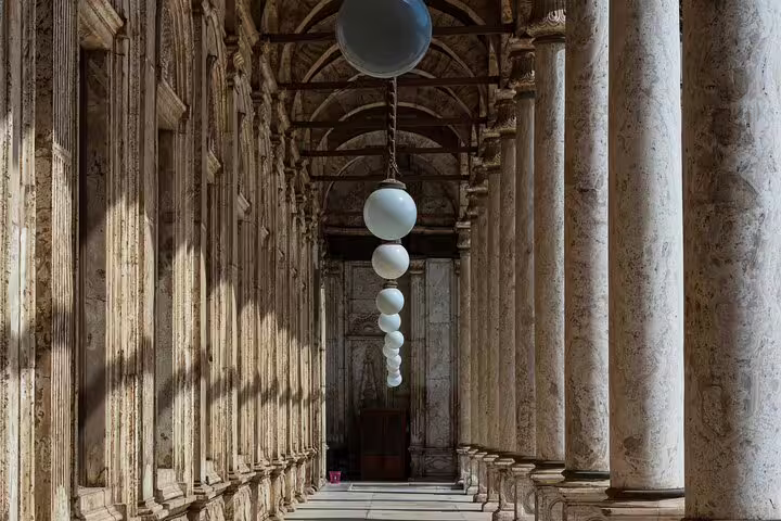 Stone colonnade inside a historic Cairo mosque with hanging lamps, guided tour of Islamic Cairo landmarks