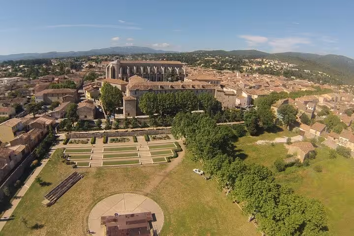 Aerial view of a historic church and gardens in the picturesque village of Provence, surrounded by lush countryside.