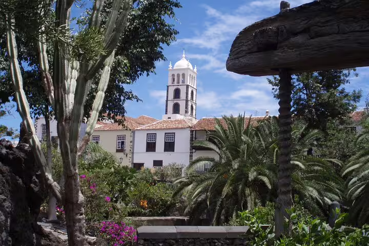 Beautiful view of a historic church tower surrounded by lush gardens in Icod, Tenerife under a clear blue sky.