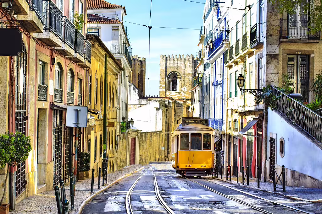 Historic Lisbon street with a vintage yellow tram passing by colorful buildings and a view of the iconic Lisbon Cathedral.
