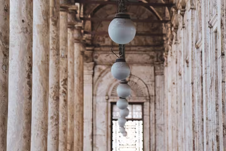 Arched mosque corridor with hanging lamps and marble columns in Islamic Cairo on a guided heritage tour