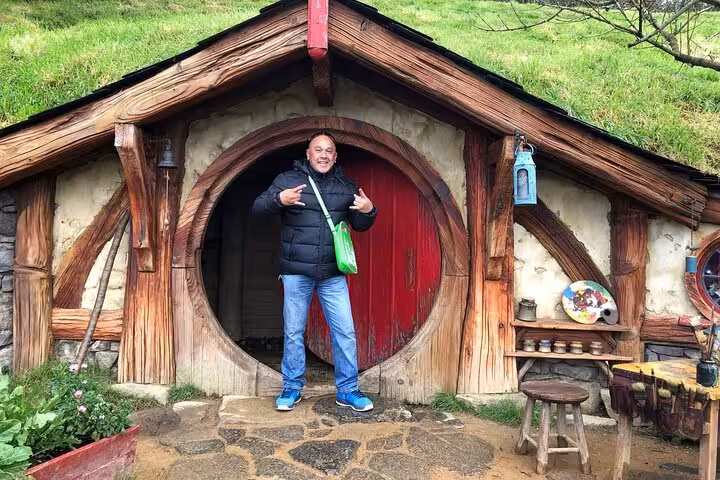 Visitor enjoying a photo opportunity at an iconic Hobbit house entrance on the Hobbiton Movie Set Day Tour.