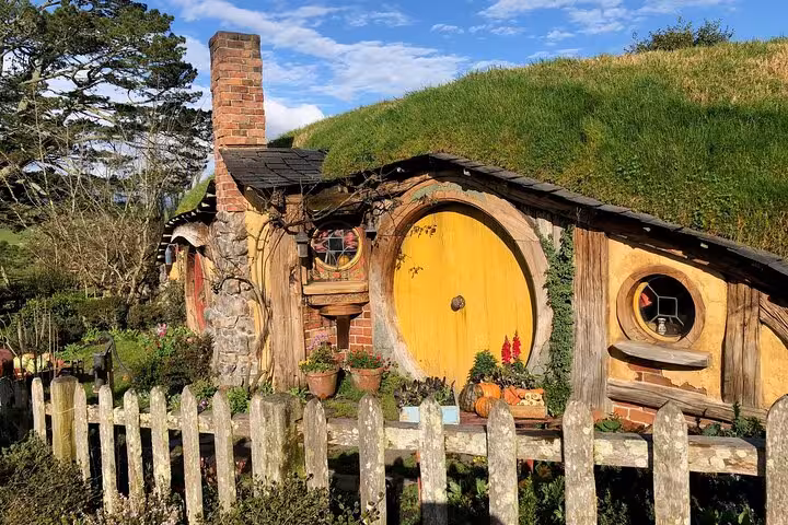 Picturesque Hobbiton house with a yellow door and lush surroundings, a must-see on the movie set tour.