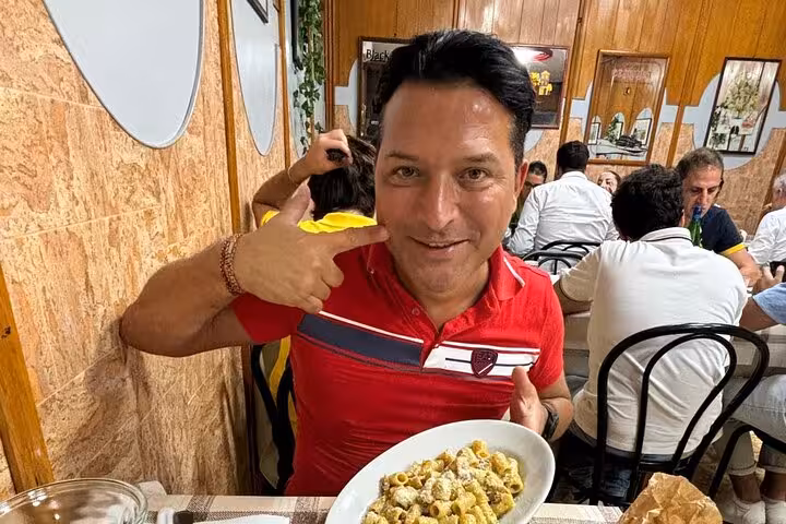 Man enjoying a plate of homemade pasta in a cozy Roman restaurant during a private cooking class experience.