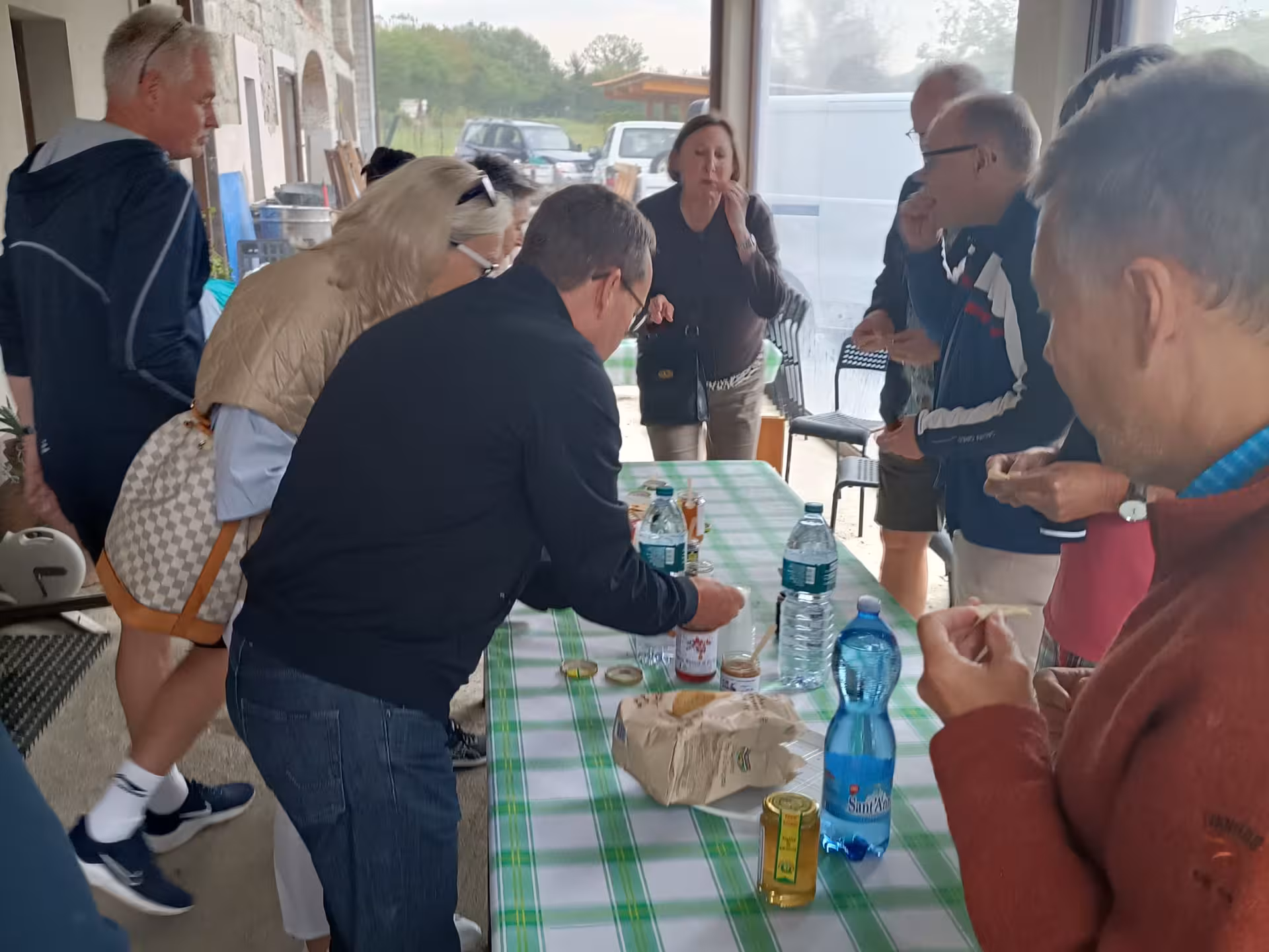 Group enjoying honey and mead tasting at a Monferrato farm with various jars and bottles on a checkered table.