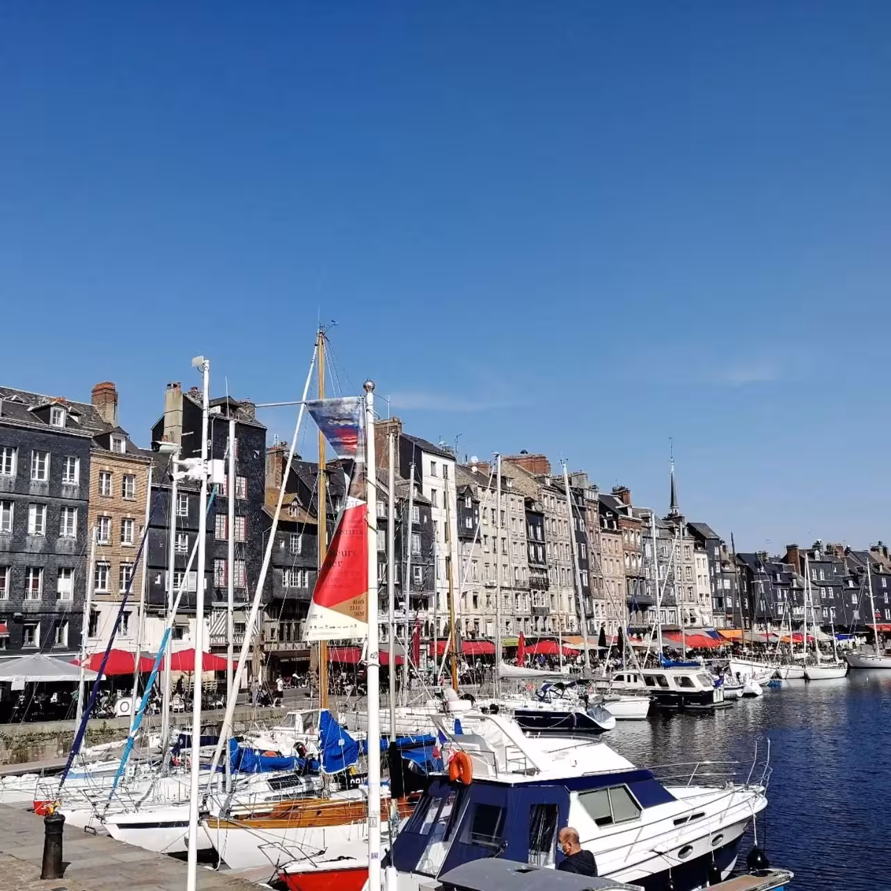 Honfleur harbor with sailboats and waterfront cafés, a coastal highlight near Deauville on Normandy bike tour