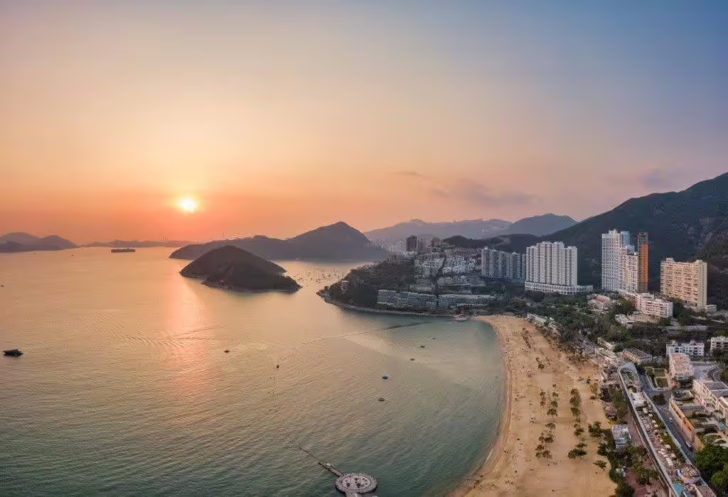 A stunning sunset view over Repulse Bay Beach, Hong Kong, showcasing urban skyline and serene waters.