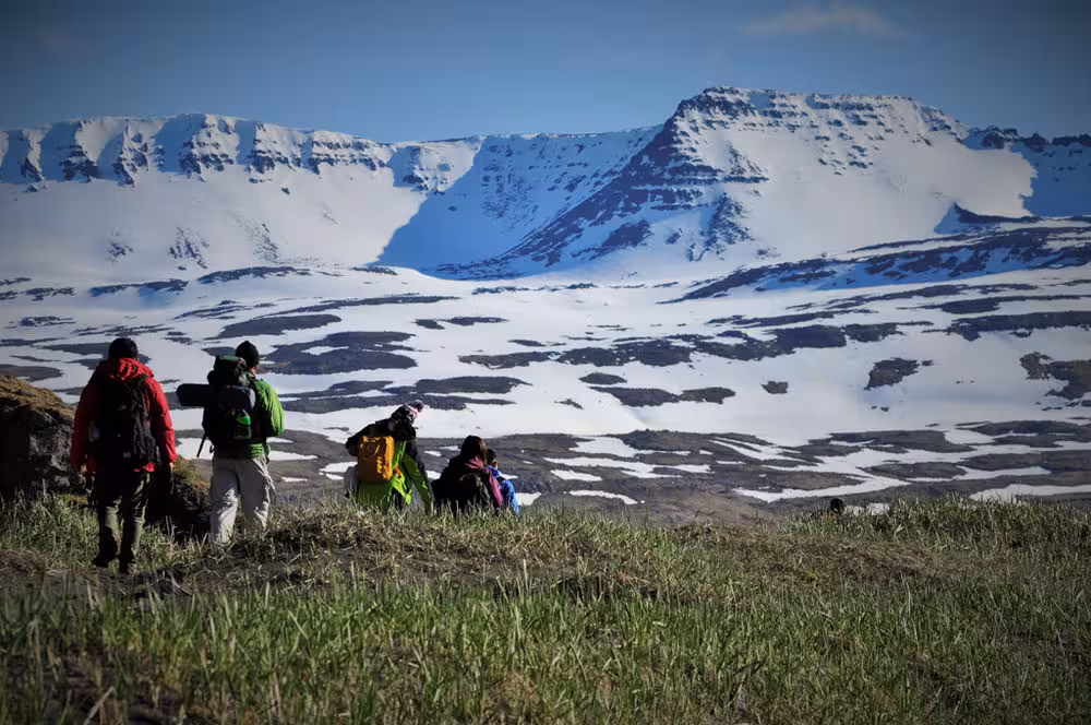 Backpackers trekking toward snow-covered peaks in Hornstrandir Nature Reserve, Iceland on the Hornstrandir Traverse