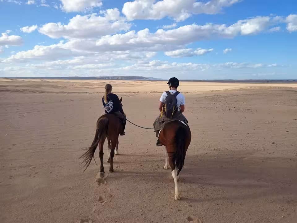 Two riders on horseback crossing Hurghada desert on a 2-hour tour with one hour sea ride and one hour desert ride