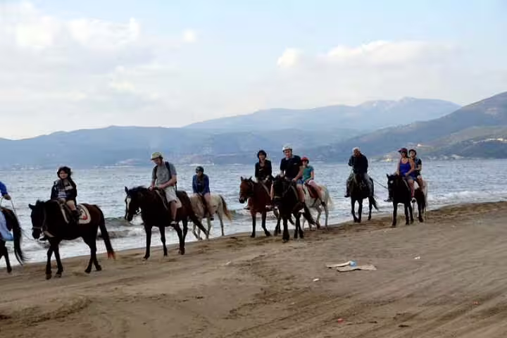 Group of tourists on horseback along a sandy beach near Kusadasi, with stunning sea and mountain views.