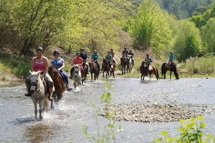 Group of riders cross a shallow stream on horseback during an adventurous tour from Kusadasi Port, ideal for cruise visitors.