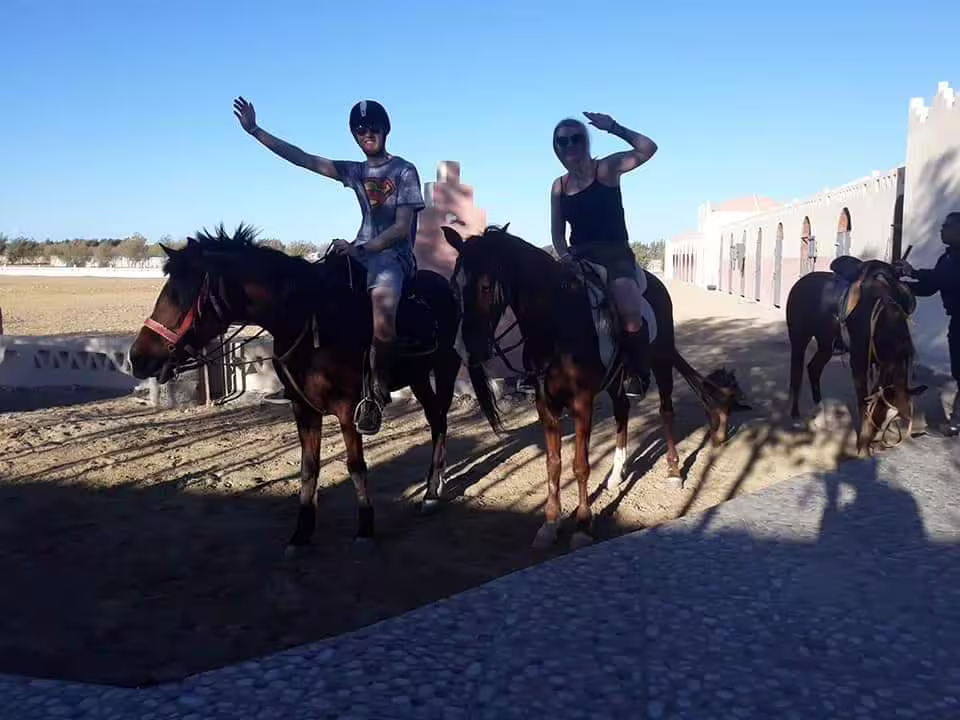 Happy riders waving on guided horseback riding in Marsa Alam desert stable yard under clear blue sky