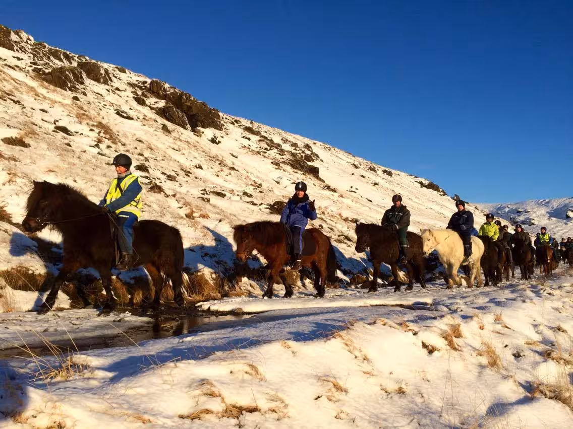 Group horseback riding past snow-covered mountain slopes under blue sky on the “03A - Meadows and Mountains” tour
