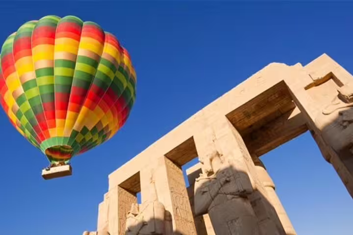 Colorful hot air balloon floating past Karnak Temple statues in Luxor, Egypt sunrise balloon tour