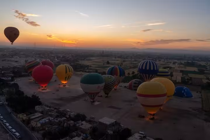Dawn hot air balloon flight in Luxor with multiple balloons inflating, including hotel pickup and drop-off service