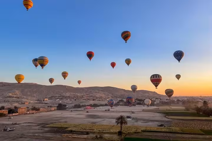 Multiple hot air balloons floating above Luxor desert at dawn, scenic West Bank flight with hotel transfers