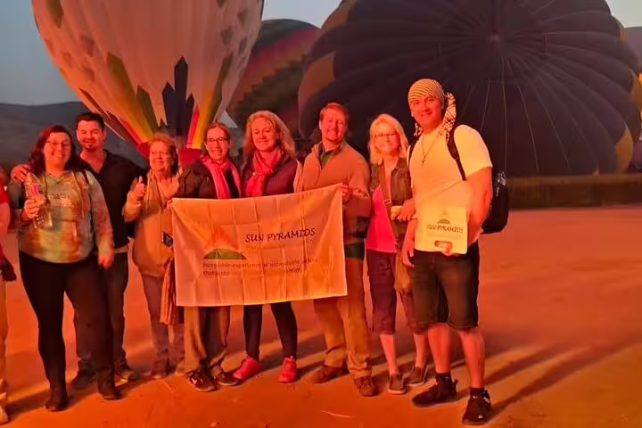 Travelers pose with pilot beside hot air balloons at sunrise in Luxor, Egypt, before a Nile Valley flight