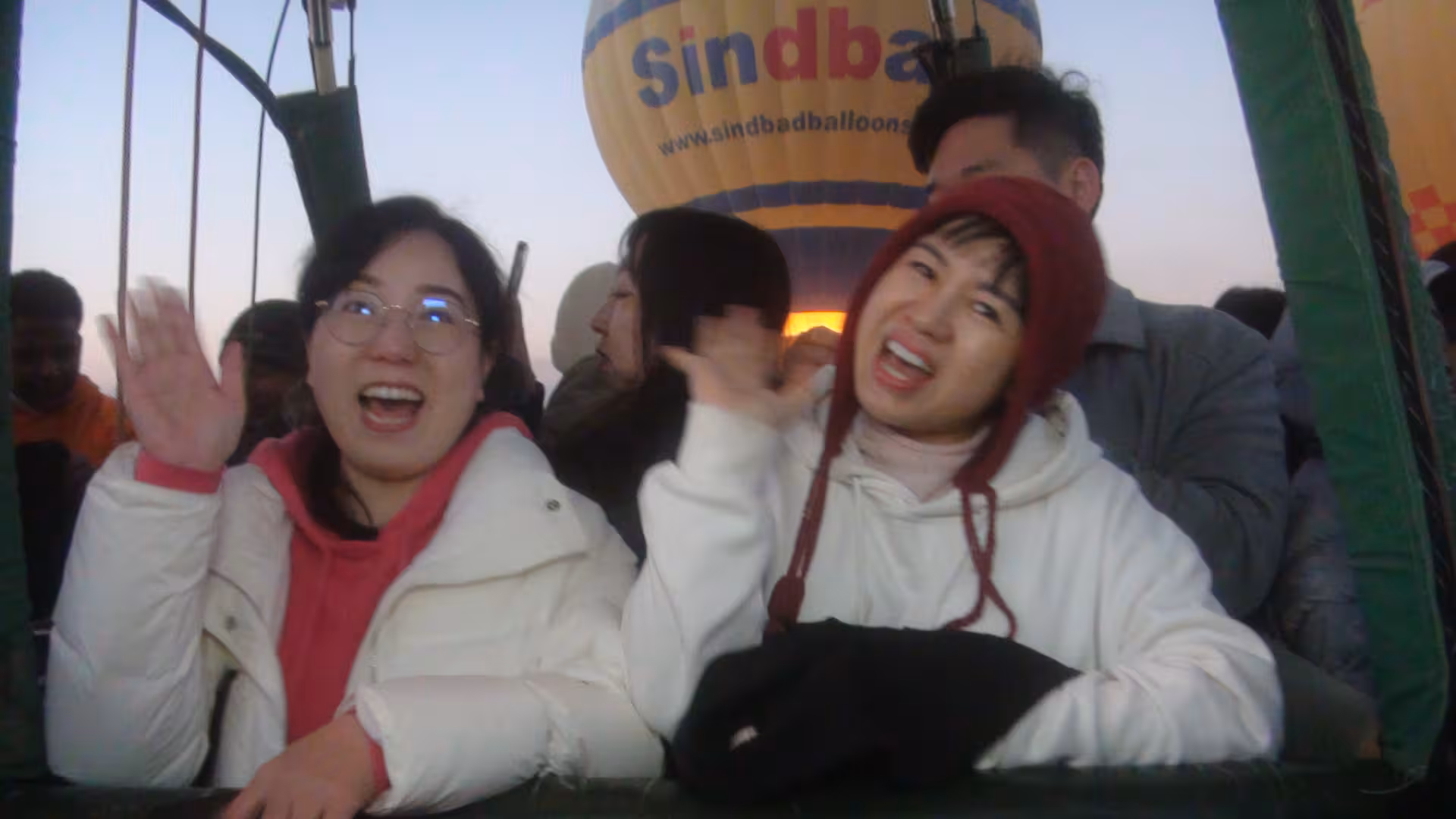 Excited tourists waving from a hot air balloon over the scenic landscapes of Luxor, Egypt, during a 15-day tour.