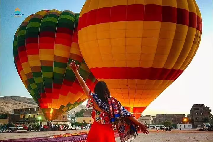 Traveler waving beside colorful hot air balloons at sunrise, Luxor Egypt balloon ride launch site