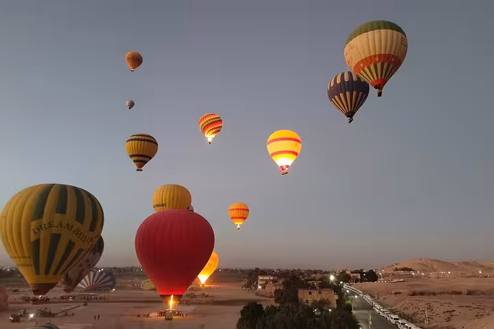 Colorful hot air balloons ascend over Luxor's West Bank at sunrise, offering a stunning panoramic view of the landscape.