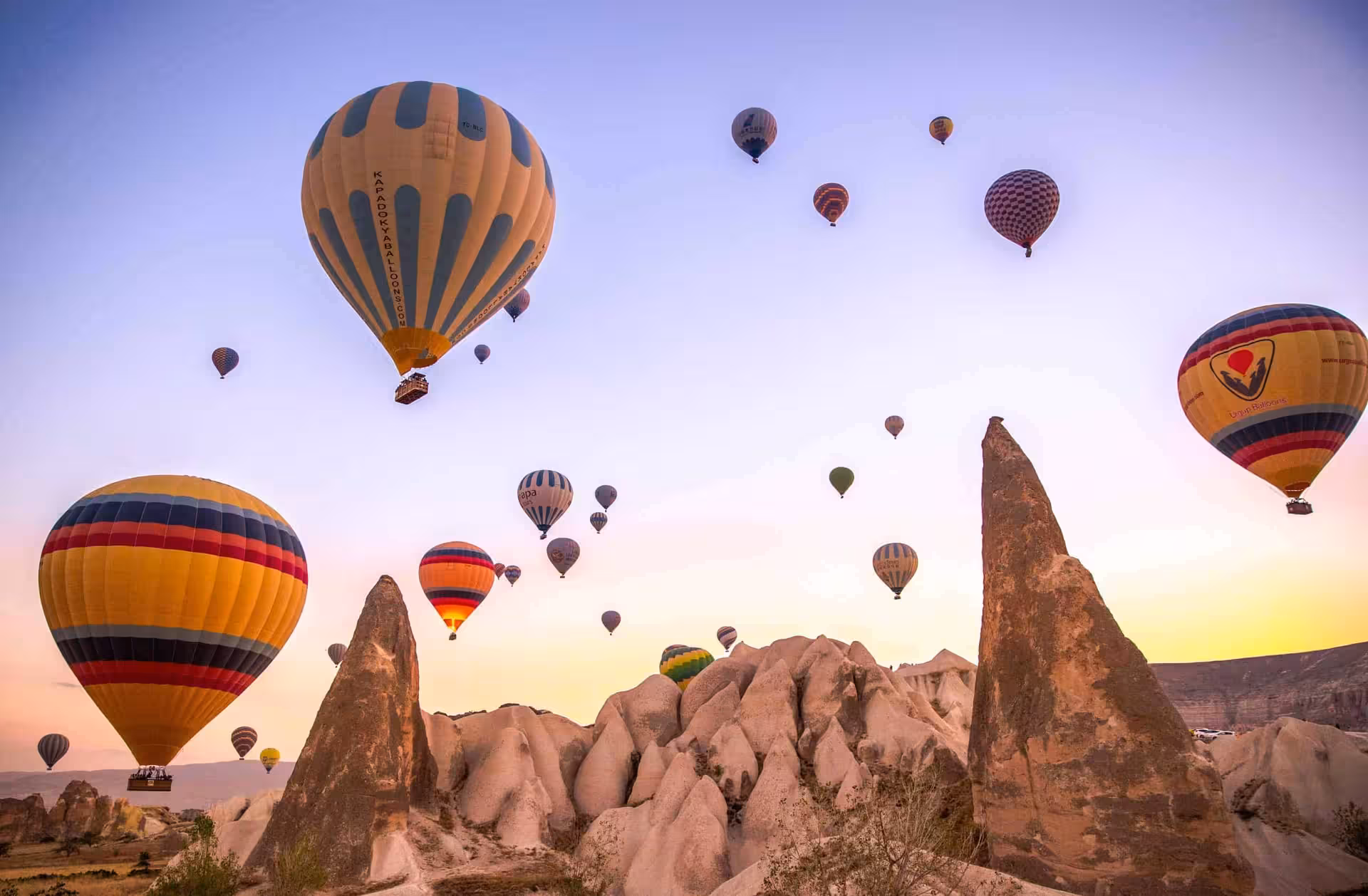 Hot air balloons drifting above a rocky Cappadocia valley with tall stone formations
