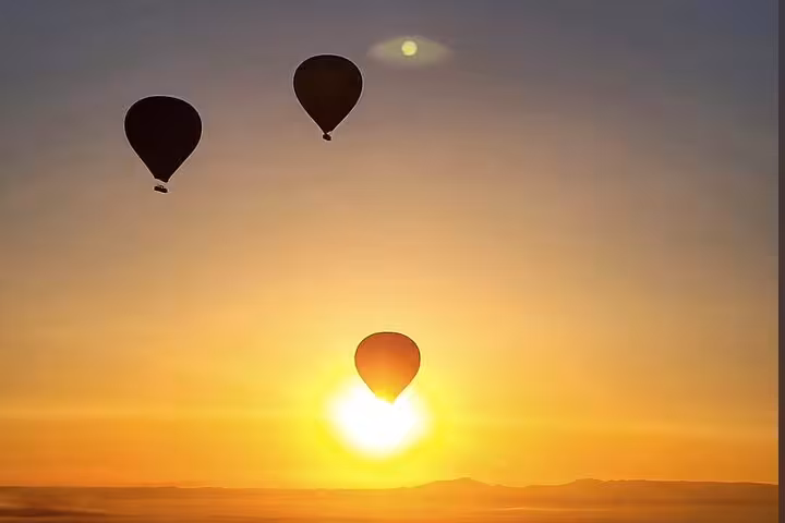 Three hot air balloons soar above Luxor West Bank at sunrise, offering a breathtaking aerial view of the Egyptian landscape.