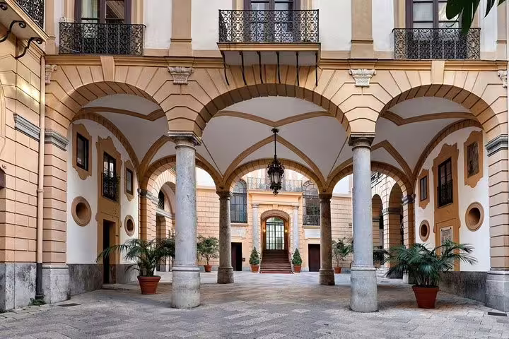 Elegant arched courtyard of Hotel Ambasciatori Palermo with columns and potted palms, ideal departure point for airport transfer