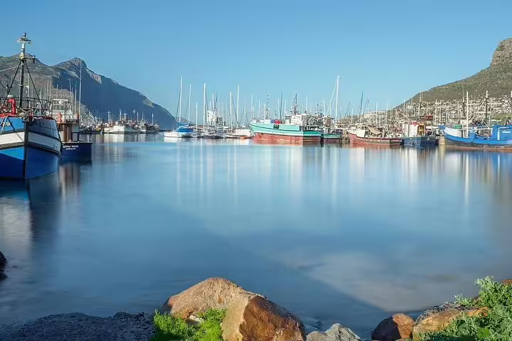 Scenic view of Hout Bay harbor with colorful boats against a mountainous backdrop on a clear day in Cape Town.