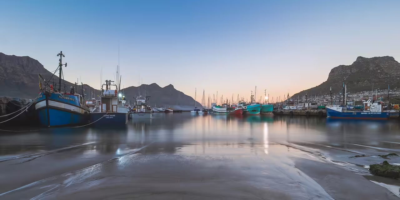 Picturesque Hout Bay harbor at sunrise with colorful fishing boats, part of Cape Town's scenic coastal tour.