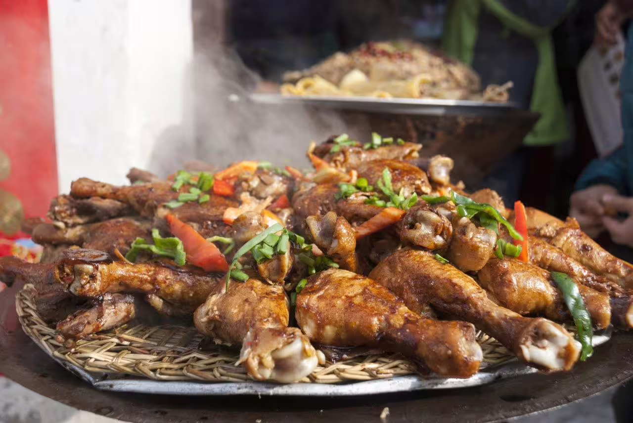 Sizzling platter of spiced chicken drumsticks garnished with fresh herbs, capturing the flavors of Huangshan street food.