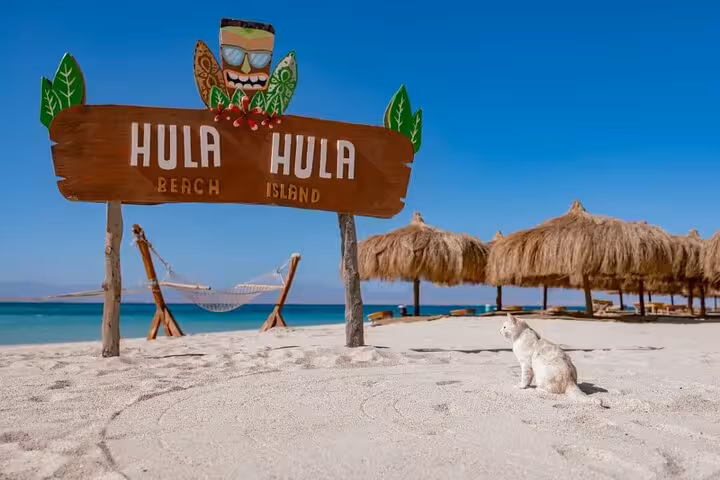 Hula Hula Island beach sign on white sand with hammocks and straw umbrellas, Hurghada sea trip stop