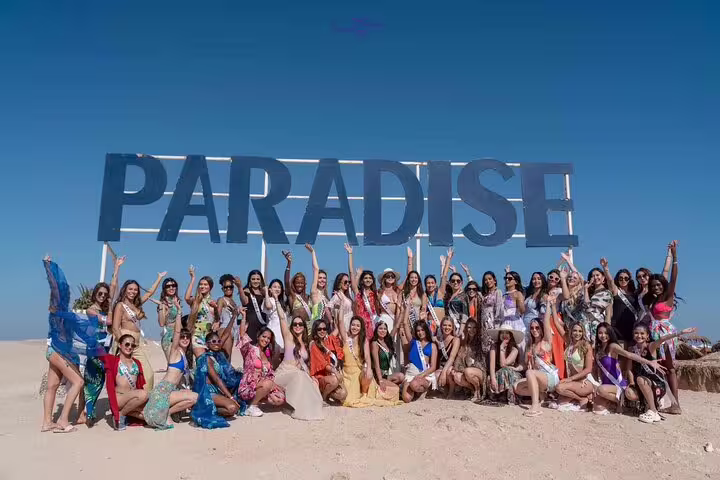 Tourists posing under PARADISE sign on Hula Hula Island beach, VIP boat day trip from Hurghada
