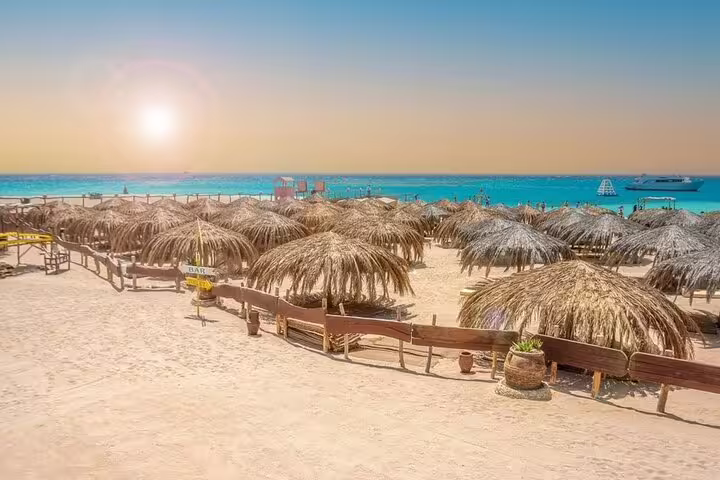 Straw sun umbrellas on Hula Hula Island sandy beach, Red Sea snorkeling day trip by VIP boat from Hurghada