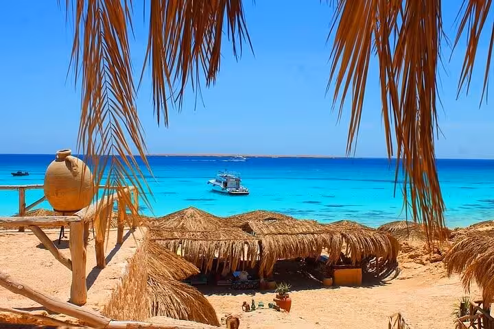 Turquoise Red Sea view from Hula Hula Island Hurghada with palm shade huts and boat anchoring offshore