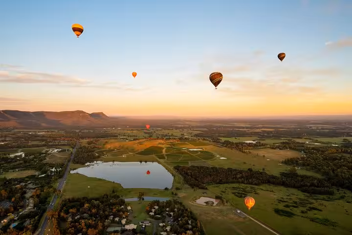 Scenic view of hot air balloons floating over Hunter Valley landscape at sunrise, perfect for private wine tours.