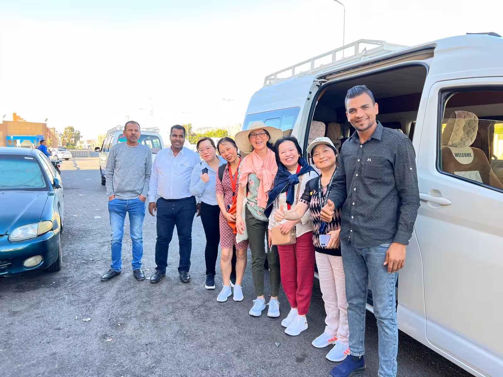 Group of tourists with driver beside white minibus for Hurghada Airport transfer, comfortable shuttle pickup